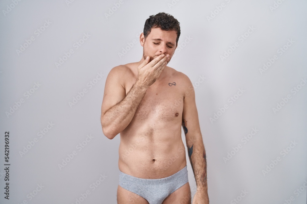 Young hispanic man standing shirtless wearing underware bored yawning tired covering mouth with hand. restless and sleepiness.