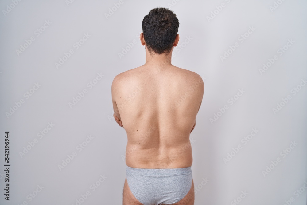 Fototapeta premium Young hispanic man standing shirtless wearing underware standing backwards looking away with crossed arms