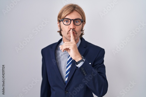 Caucasian man with mustache wearing business clothes asking to be quiet with finger on lips. silence and secret concept.