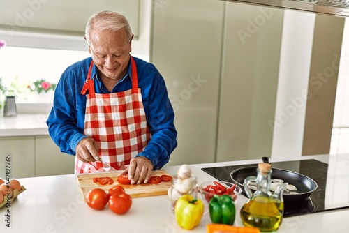 Senior man smiling confident cutting tomato at kitchen