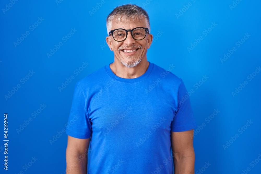 Hispanic man with grey hair standing over blue background with a happy and cool smile on face. lucky person. Hispanic man with grey hair standing over blue background with a happy and cool smile on face. lucky person.