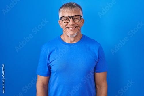 Hispanic man with grey hair standing over blue background with a happy and cool smile on face. lucky person. © Krakenimages.com