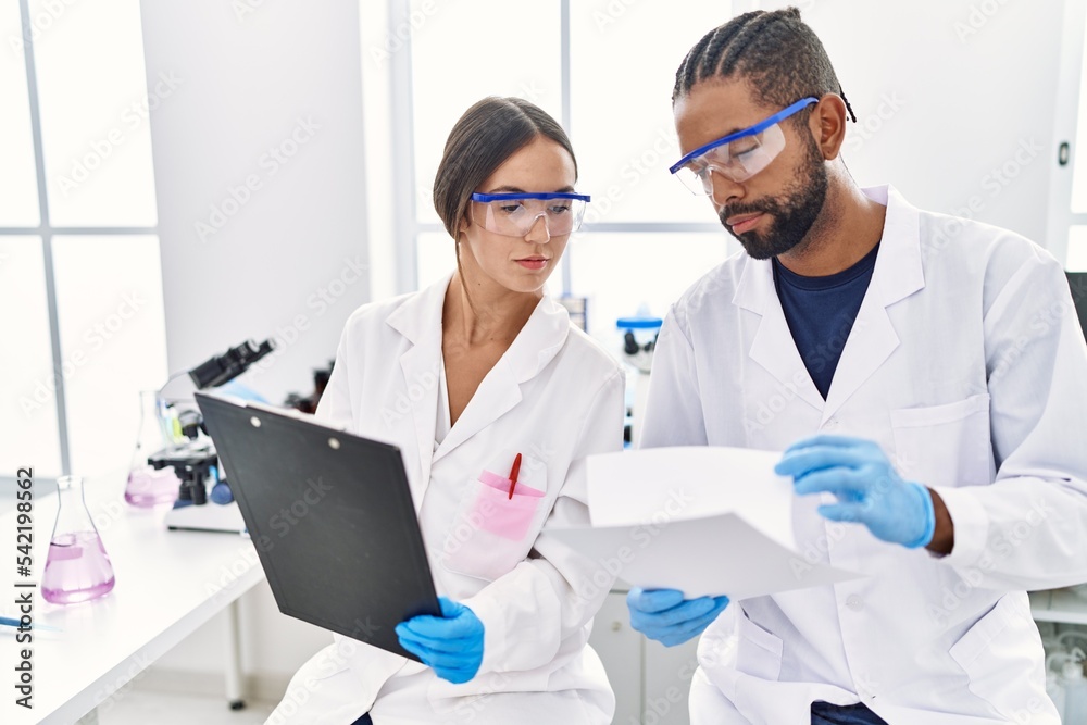 Man and woman scientist partners reading documents at laboratory Man and woman scientist partners reading documents at laboratory