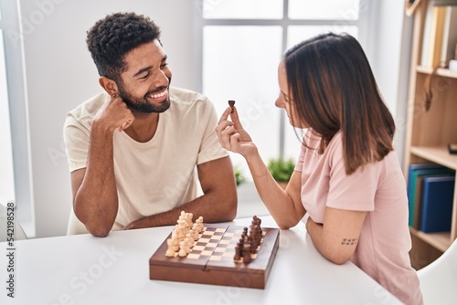 Man and woman couple sitting on table playing chess at home
