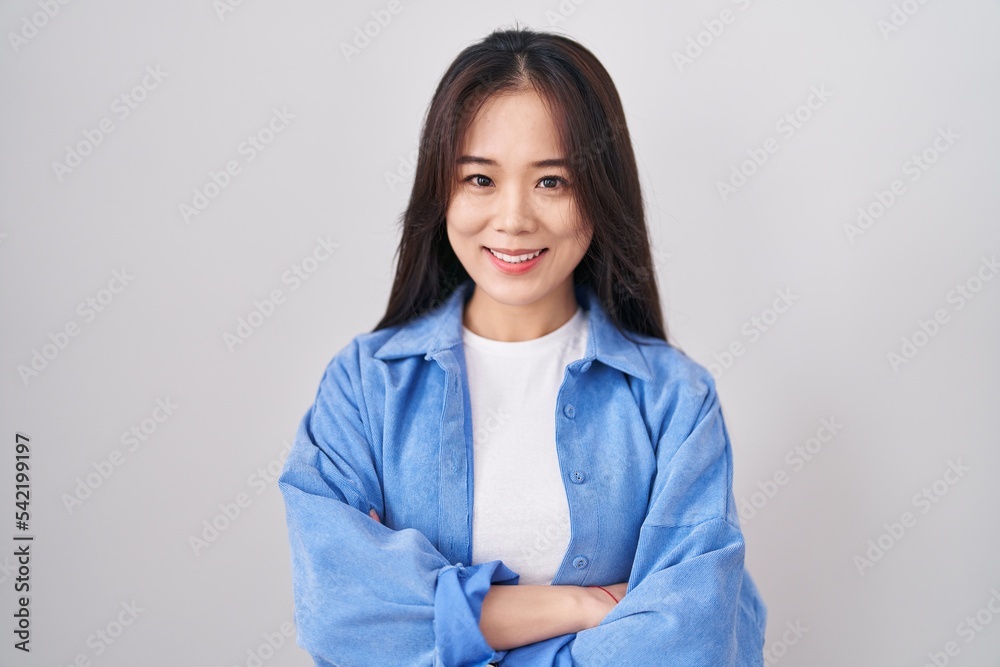Young chinese woman standing over white background happy face smiling with crossed arms looking at the camera. positive person. Young chinese woman standing over white background happy face smiling with crossed arms looking at the camera. positive person.
