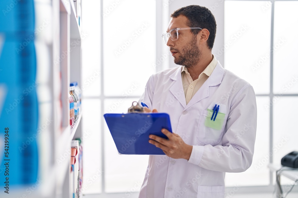 © Krakenimages.com - Young man pharmacist writing on document organize shelving at pharmacy