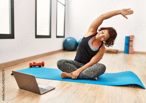 Middle age hispanic sporty woman having online fitness class at sport center.