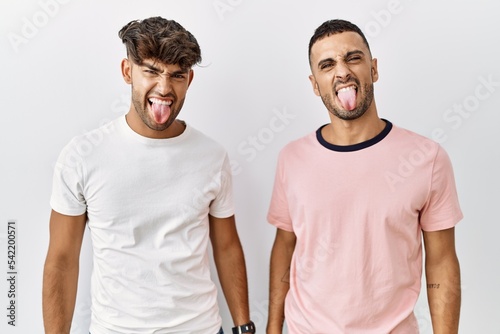 Young gay couple standing over isolated background sticking tongue out happy with funny expression. emotion concept.
