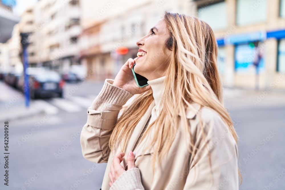 Fototapeta premium Young blonde woman smiling confident talking on smartphone at street