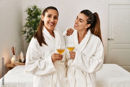 Two women wearing bathrobe toasting with champagne standing at beauty center