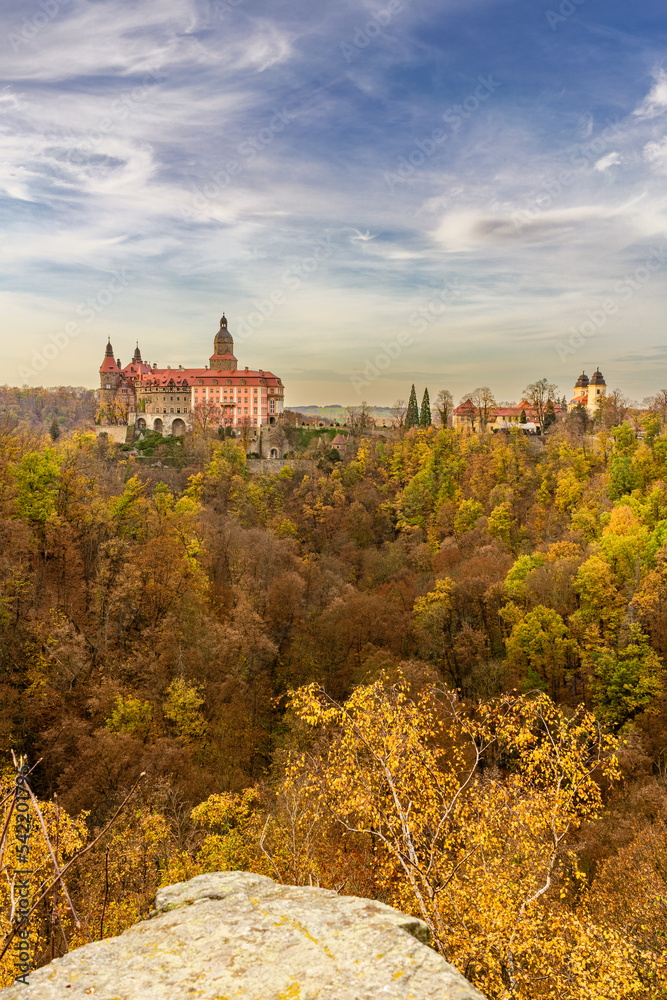 A photo of Książ Castle in Wałbrzych set against a beautiful autumn sky. The castle, with its impressive architecture, stands out against the picturesque background of the colorful fall foliage