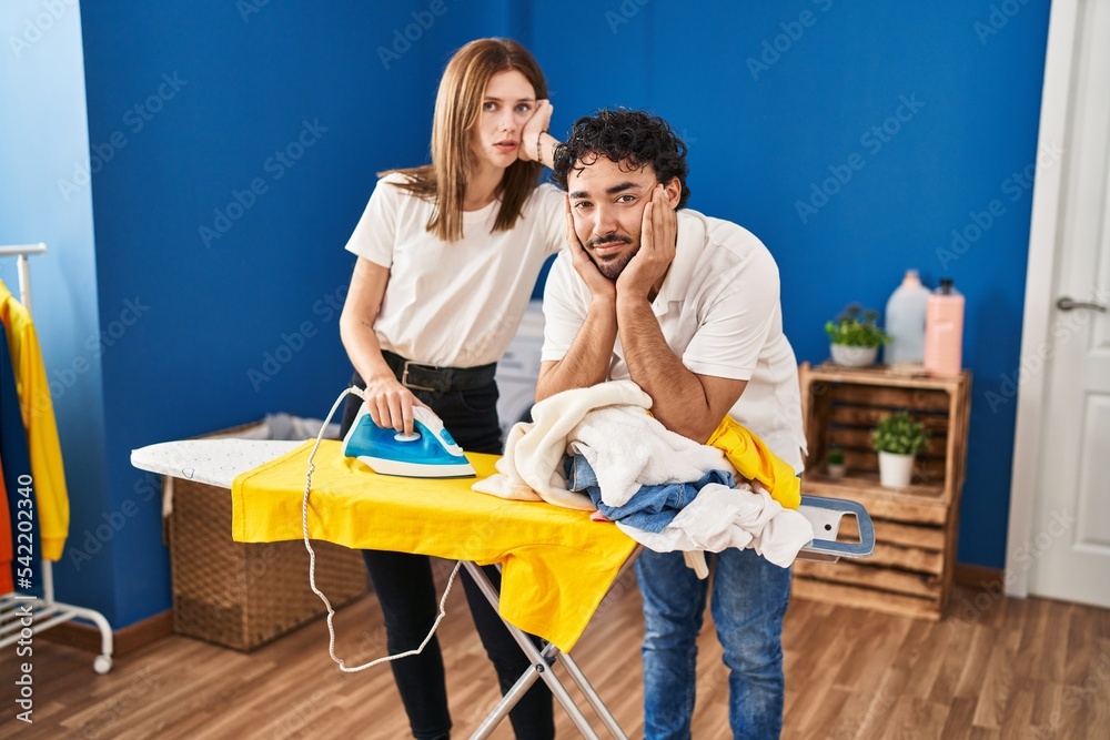 Man and woman couple with tired expression ironing at laundry room Man and woman couple with tired expression ironing at laundry room