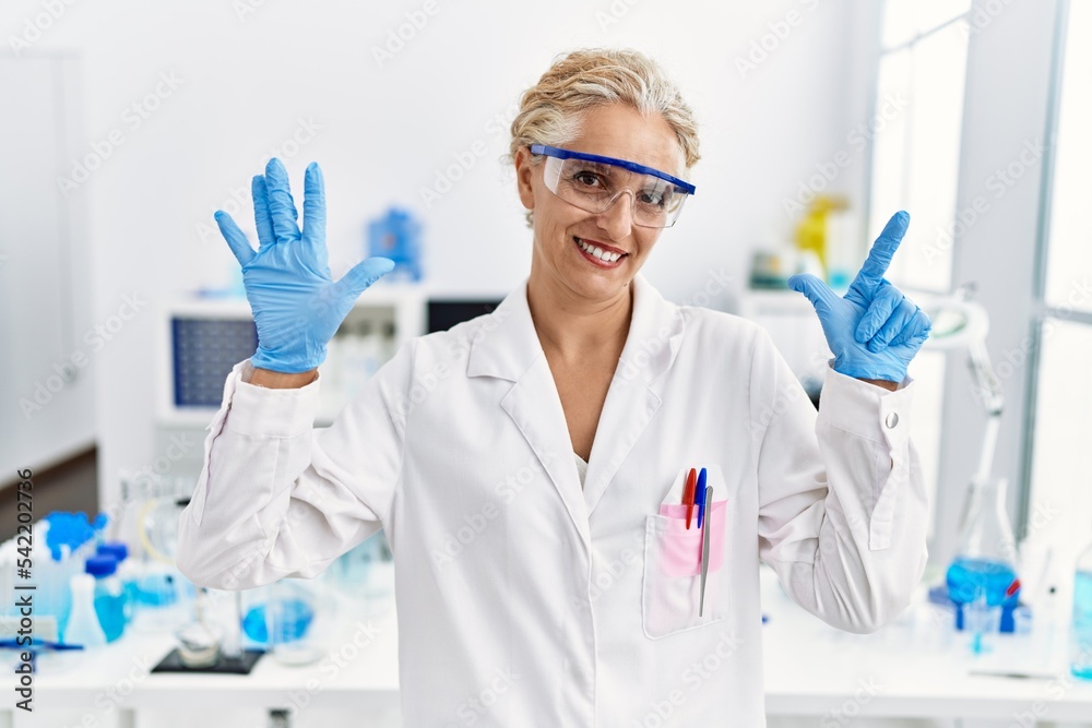 Middle age blonde woman working at scientist laboratory showing and pointing up with fingers number seven while smiling confident and happy. Middle age blonde woman working at scientist laboratory showing and pointing up with fingers number seven while smiling confident and happy.