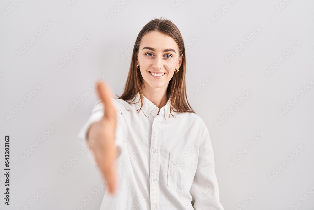 Young caucasian woman standing over isolated background smiling friendly offering handshake as greeting and welcoming. successful business. Young caucasian woman standing over isolated background smiling friendly offering handshake as greeting and welcoming. successful business.