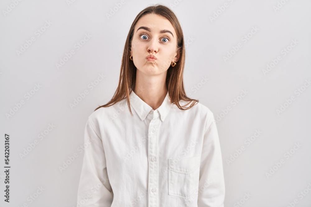 Young caucasian woman standing over isolated background puffing cheeks with funny face. mouth inflated with air, crazy expression. Young caucasian woman standing over isolated background puffing cheeks with funny face. mouth inflated with air, crazy expression.