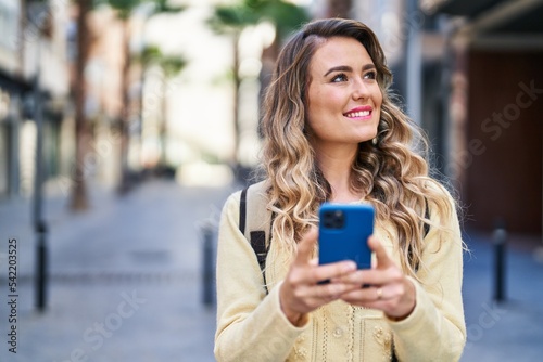 Young woman tourist smiling confident using smartphone at street