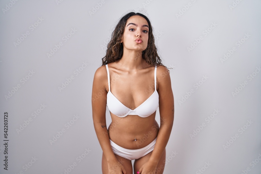 Young hispanic woman wearing white lingerie looking at the camera blowing a kiss on air being lovely and sexy. love expression. Young hispanic woman wearing white lingerie looking at the camera blowing a kiss on air being lovely and sexy. love expression.