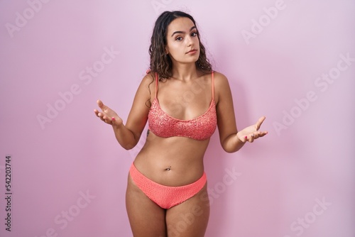 Young hispanic woman wearing lingerie over pink background clueless and confused with open arms, no idea concept.