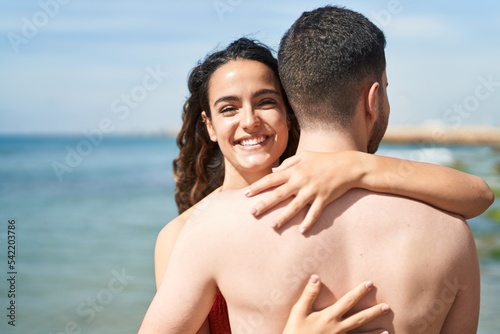 Young hispanic couple tourists wearing swimsuit hugging each other at seaside