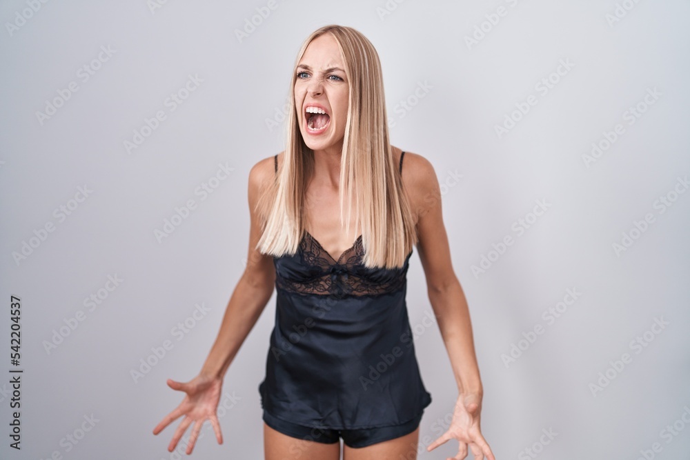 Young caucasian woman wearing nightgown angry and mad screaming frustrated and furious, shouting with anger. rage and aggressive concept. Young caucasian woman wearing nightgown angry and mad screaming frustrated and furious, shouting with anger. rage and aggressive concept.
