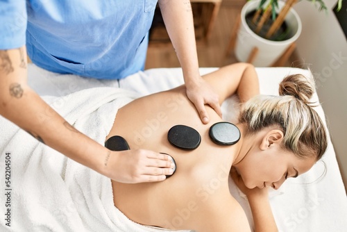 Woman couple having back treatment using hot black stones at beauty center photo