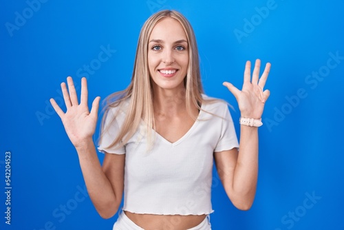 Young caucasian woman standing over blue background showing and pointing up with fingers number nine while smiling confident and happy.