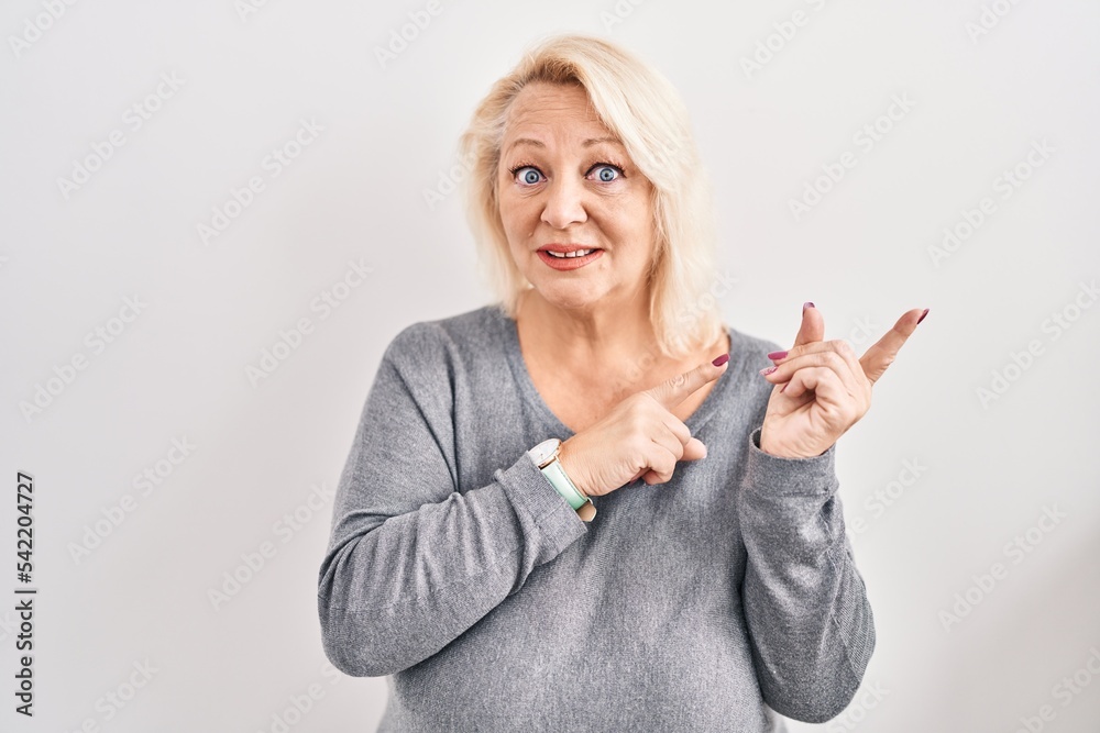 Middle age caucasian woman standing over white background pointing aside worried and nervous with both hands, concerned and surprised expression Middle age caucasian woman standing over white background pointing aside worried and nervous with both hands, concerned and surprised expression