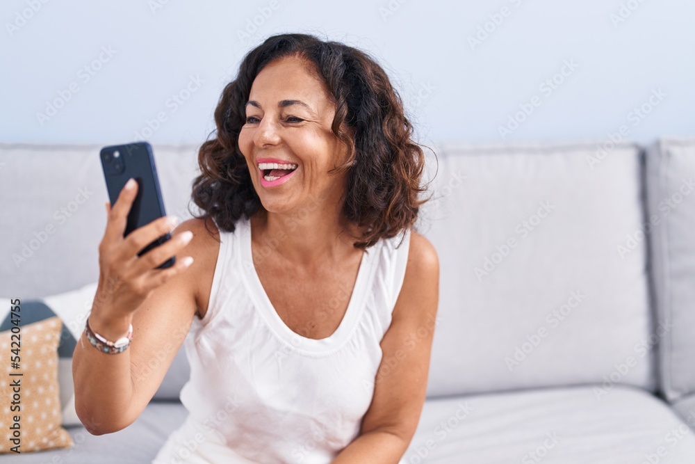 Middle age woman having video call sitting on table at home Middle age woman having video call sitting on table at home