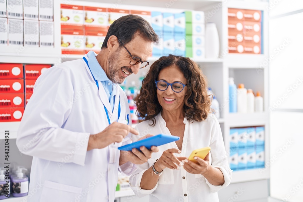 Man and woman pharmacists using touchpad and smartphone working at pharmacy