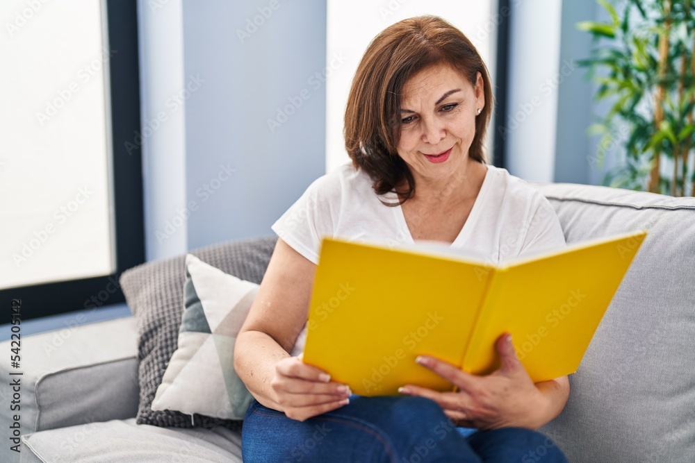 Middle age woman reading book sitting on sofa at home Middle age woman reading book sitting on sofa at home