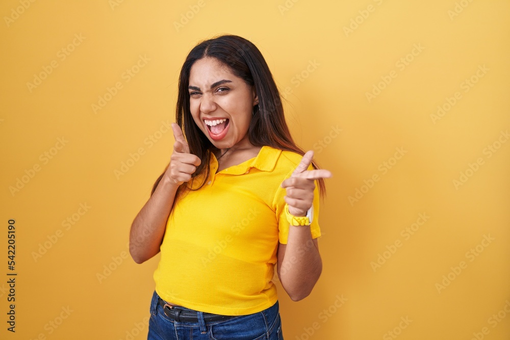 Young arab woman standing over yellow background pointing fingers to camera with happy and funny face. good energy and vibes. Young arab woman standing over yellow background pointing fingers to camera with happy and funny face. good energy and vibes.