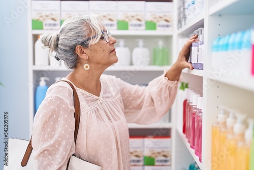 Middle age grey-haired woman customer looking shelving at pharmacy
