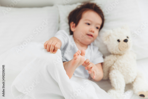 A little Asian boy in pajamas lying on the bed with a teddy bear, The child wakes up happy, The child wakes up early in the morning.natural bed linen for children