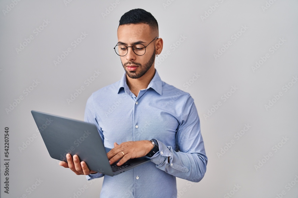 Young hispanic man working using computer laptop relaxed with serious expression on face. simple and natural looking at the camera. Young hispanic man working using computer laptop relaxed with serious expression on face. simple and natural looking at the camera.