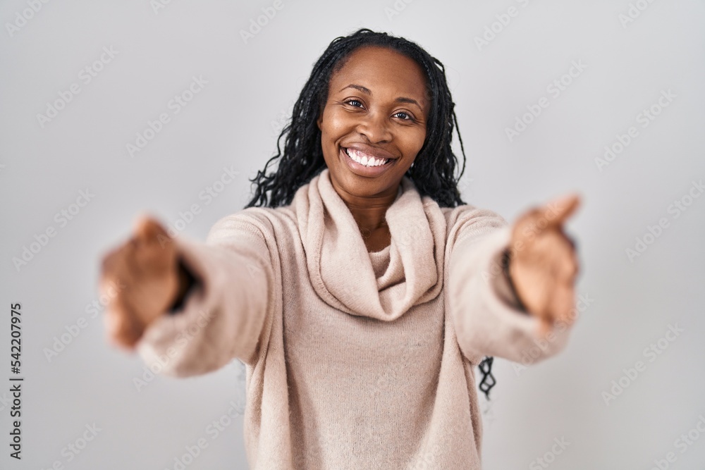 African woman standing over white background looking at the camera smiling with open arms for hug. cheerful expression embracing happiness.
