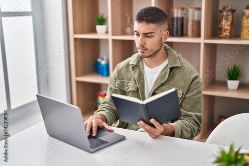Young hispanic man sitting on table studying at home