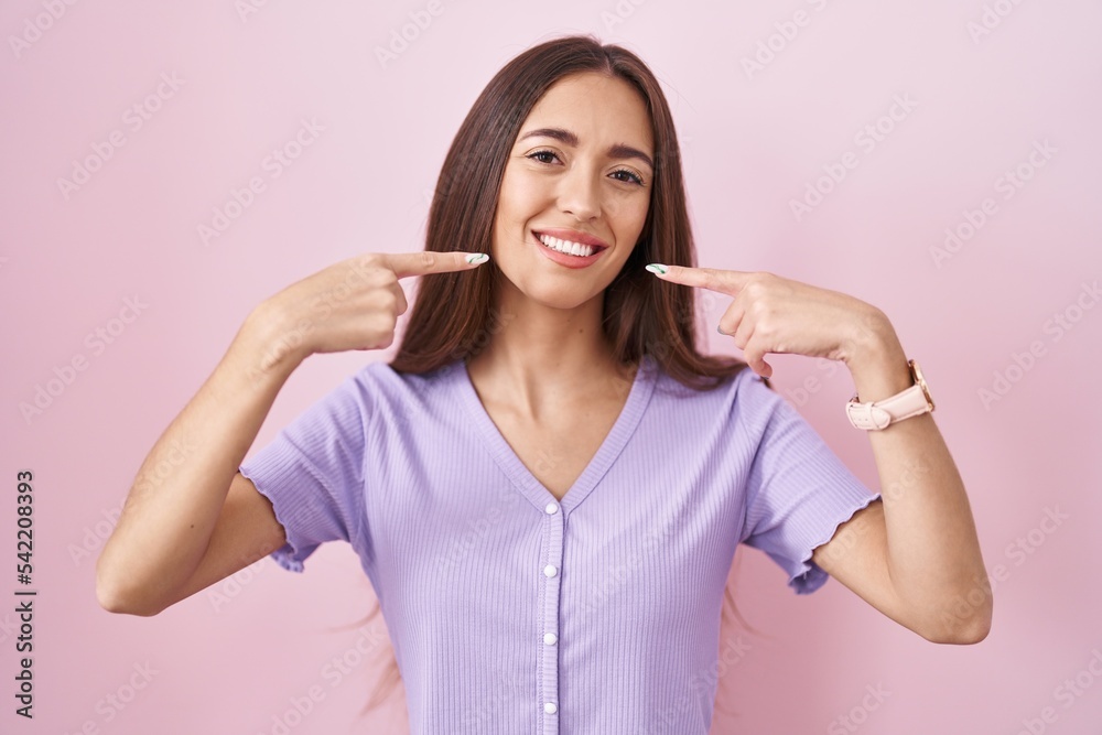 Young hispanic woman with long hair standing over pink background smiling cheerful showing and pointing with fingers teeth and mouth. dental health concept. Young hispanic woman with long hair standing over pink background smiling cheerful showing and pointing with fingers teeth and mouth. dental health concept.