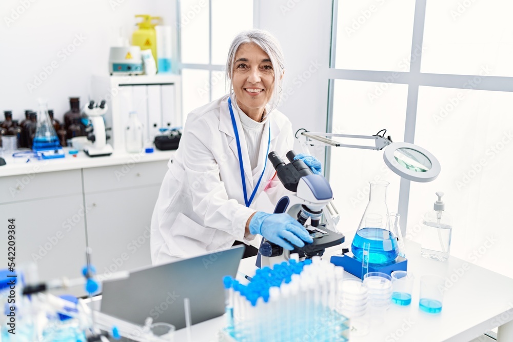 Fototapeta premium Middle age grey-haired woman wearing scientist uniform using microscope at laboratory