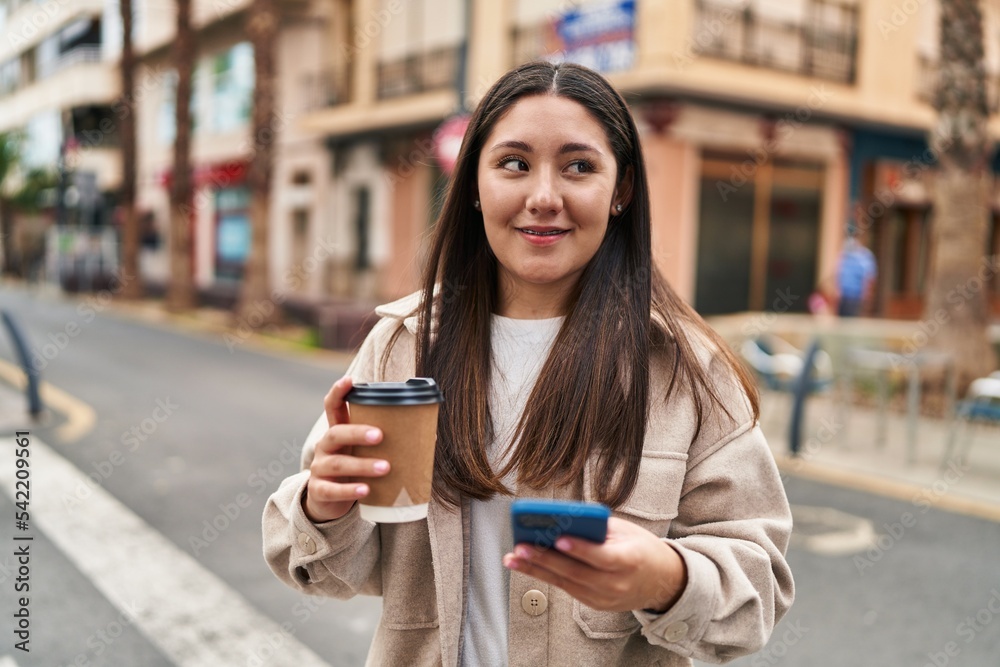 Young hispanic woman using smartphone drinking coffee at street