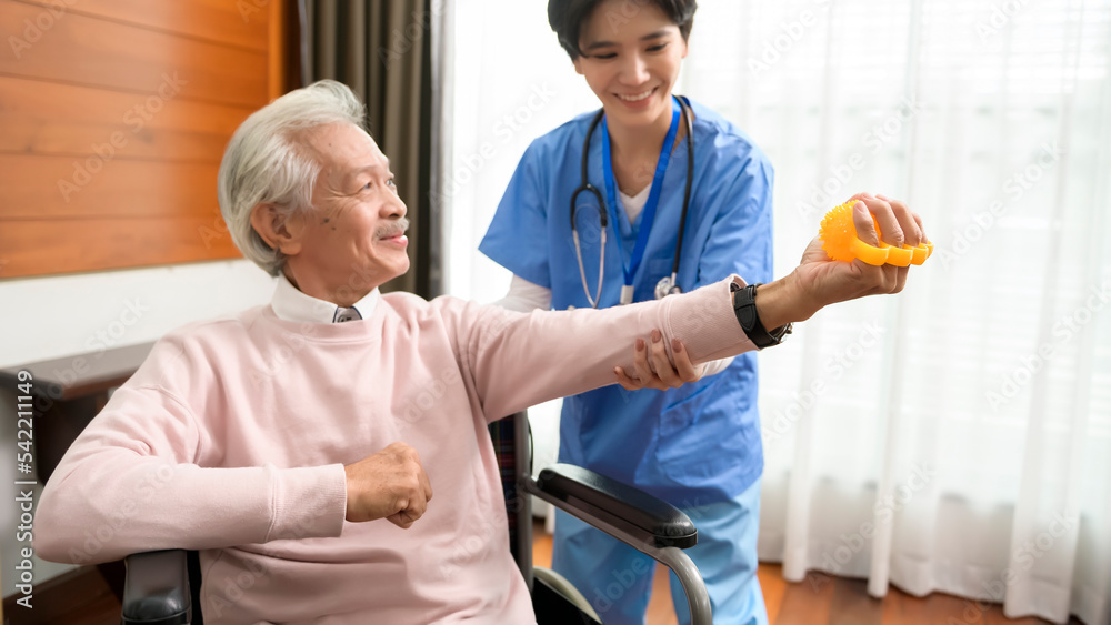 Fototapeta premium Asian nurse taking care of an elderly man sitting on wheelchair , doing hand exercises at senior healthcare center.