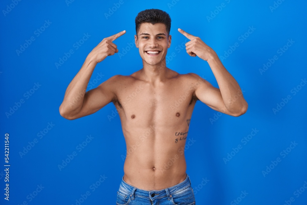 Young hispanic man standing shirtless over blue background smiling pointing to head with both hands finger, great idea or thought, good memory