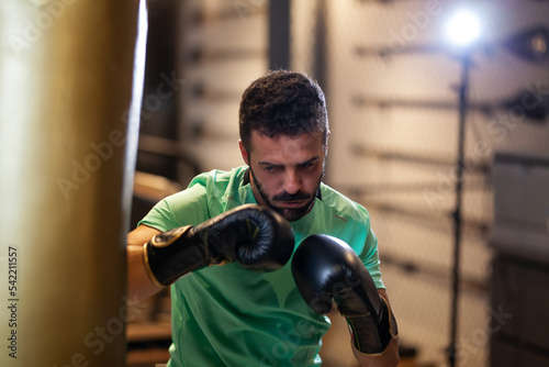 Muscular man with boxing gloves hitting a punching bag in a fitness studio. © Nikola Spasenoski