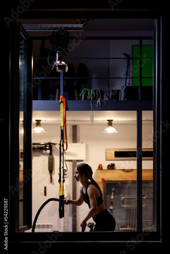 Fit girl practicing with ropes in a fitness studio. View from outsite the window.