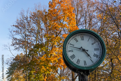 Vintage round clock face in a public park in the sunny autumn day