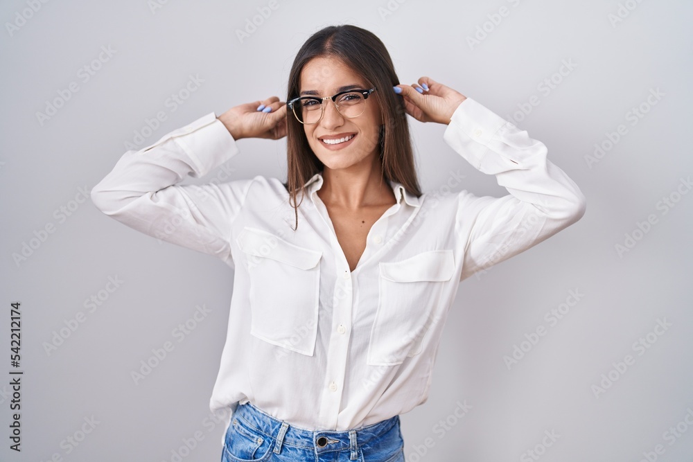 Young brunette woman wearing glasses smiling pulling ears with fingers, funny gesture. audition problem Young brunette woman wearing glasses smiling pulling ears with fingers, funny gesture. audition problem