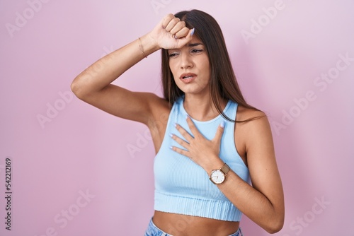 Young brunette woman standing over pink background touching forehead for illness and fever  flu and cold  virus sick