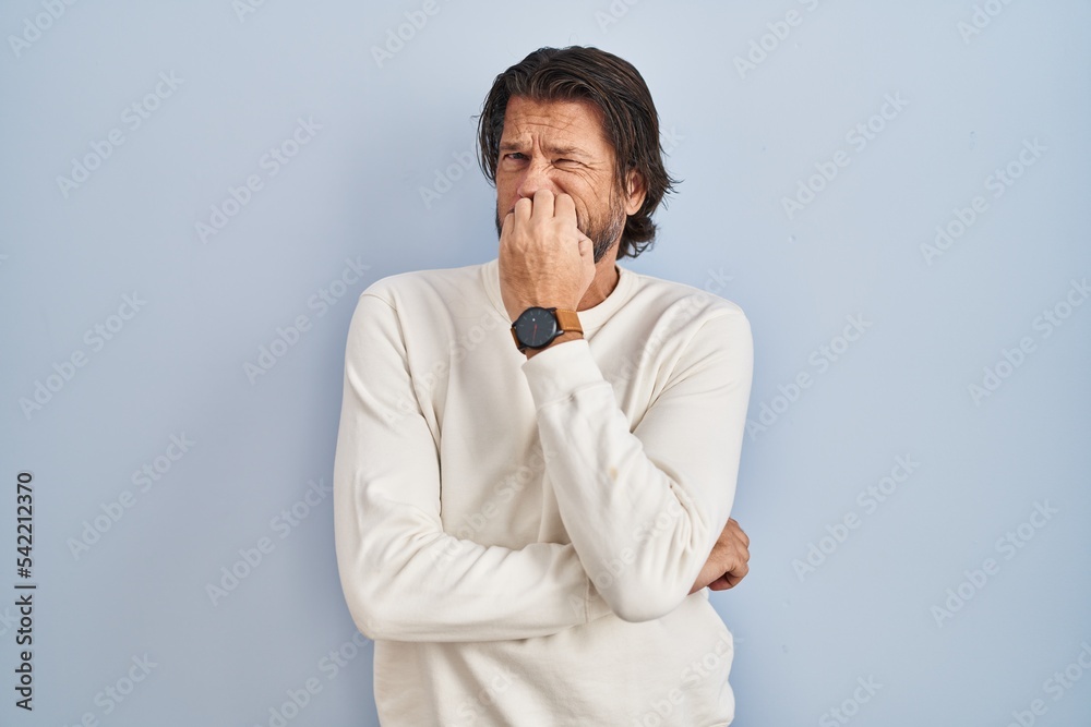 Handsome middle age man wearing casual sweater over blue background looking stressed and nervous with hands on mouth biting nails. anxiety problem. Handsome middle age man wearing casual sweater over blue background looking stressed and nervous with hands on mouth biting nails. anxiety problem.
