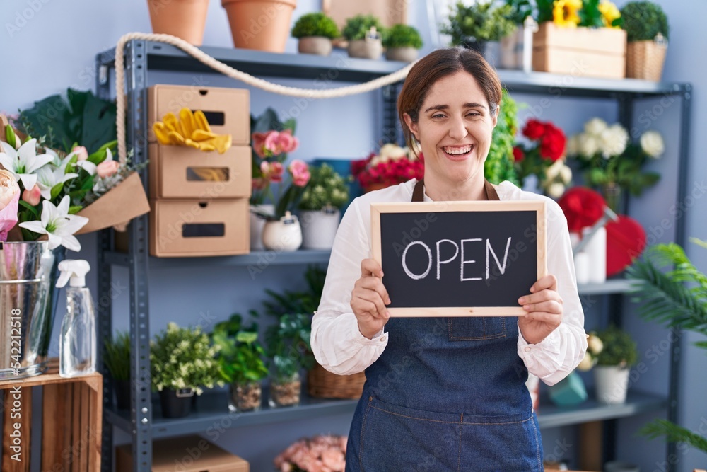 Brunette woman working at florist holding open sign smiling and laughing hard out loud because funny crazy joke. Brunette woman working at florist holding open sign smiling and laughing hard out loud because funny crazy joke.