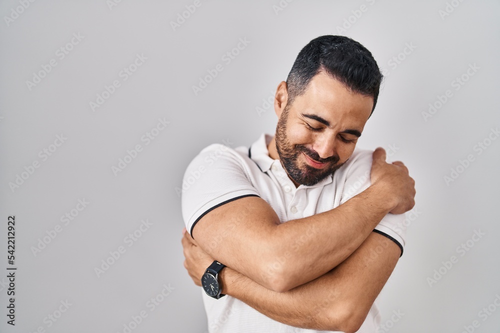 Young hispanic man with beard wearing casual clothes over white background hugging oneself happy and positive, smiling confident. self love and self care Young hispanic man with beard wearing casual clothes over white background hugging oneself happy and positive, smiling confident. self love and self care