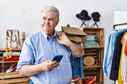 Middle age grey-haired man using smartphone shopping at clothing store